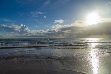 Obraz premium A wide-angle view of the Mediterranean coastline during a bright spring day, featuring dramatic clouds and sun reflections on the sea surface.