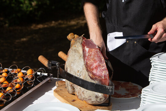 Chef carving prosciutto ham at outdoor catering buffet