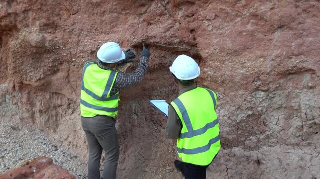 Two geologists analyzing soil and rock formations at a mining excavation site. They are conducting geological surveys and evaluating mineral resources for industrial project planning.
