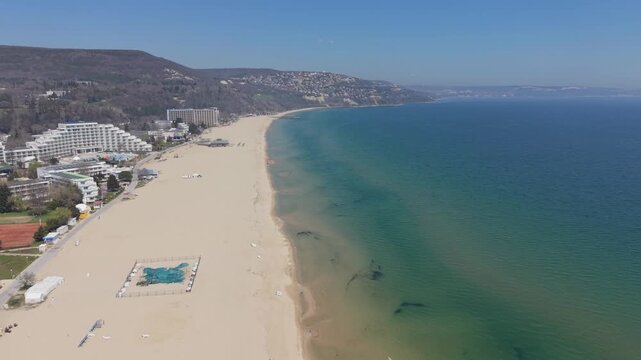 Aerial drone view of curved sandy beach with turquoise sea and distant coastal hills landscape
