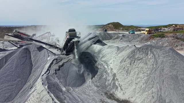 Workers use heavy machinery to extract granite and move stone at a busy quarry located near the shoreline.