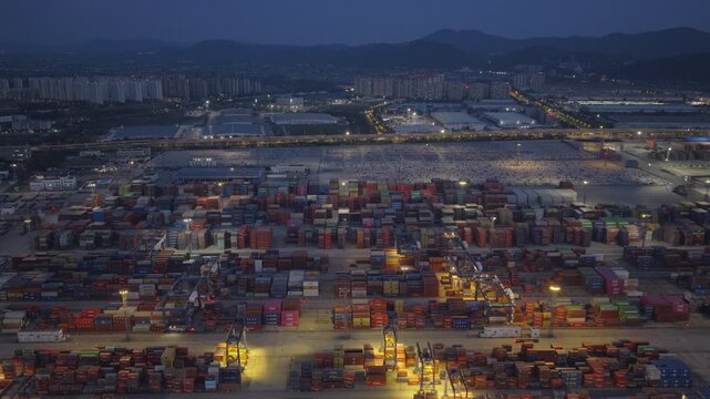 Aerial night view of illuminated container terminal and automobile yard at busy seaport