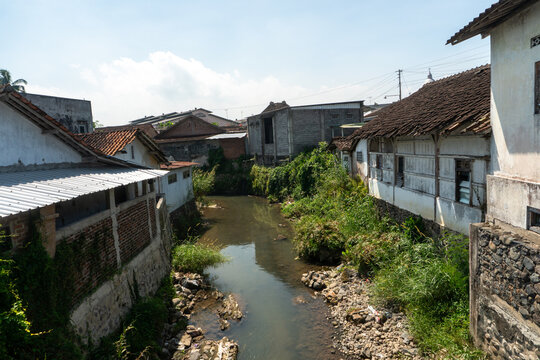 The river is bordered by densely populated settlements featuring permanent and semi-permanent houses, often with zinc roofs. This type of architecture is common throughout Southeast Asia.