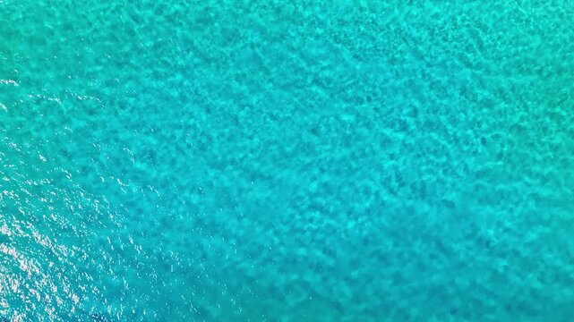 Turquoise rippling water background texture. Caribbean Sea waves on a bright sunny day. Bird's-eye view. Sea surface with reflected sunlight. Sea voyage. Water landscape.