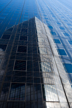 Looking upward along a glass facade, reflections sharpen office buildings into corporate architecture windows with abstract blue patterns