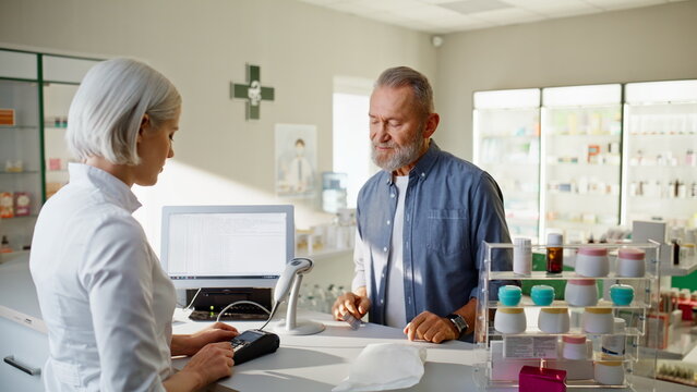 Pharmacy professional selling medicine old man cashier closeup. Customer buying