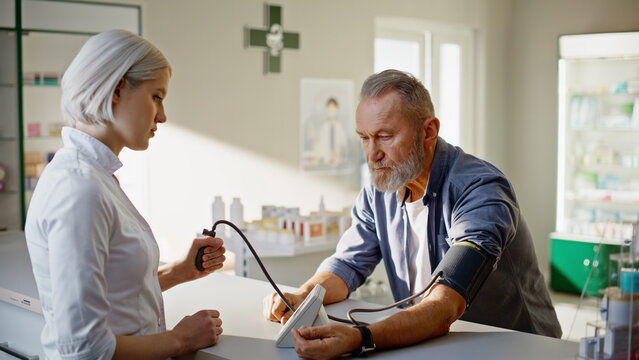 Woman pharmacist measuring blood pressure senior patient in drugstore closeup