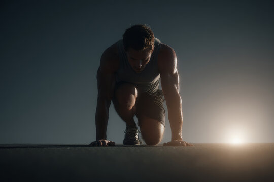 Athletic man in sportswear prepares to sprint at dawn, crouched in a starting position on an outdoor track. Focused runner readies himself for an intense early morning workout session
