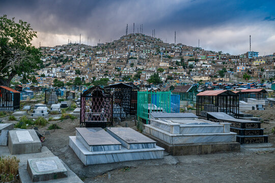 Cemetery near Blue Mosque in Kabul with graves and hillside structures under cloudy sky
