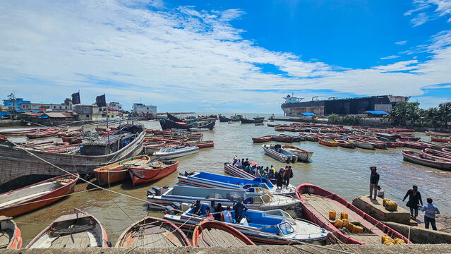 Small fishing boats gather at a shipwreck cemetery in Chittagong, Bangladesh during the day with clear skies and calm waters