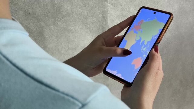Map of the world on the phone screen in the hands of a woman, a view from over the shoulder. A woman chooses a place for a summer vacation, a vacation abroad