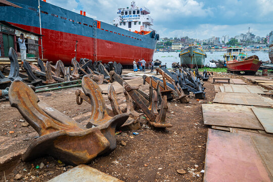 Giant anchors rest in the shipwreck yard of Dhaka while boats dock nearby along the river