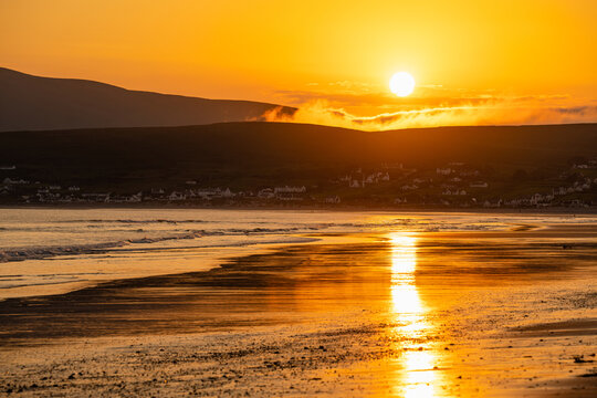 Golden sunset over Keem Beach on Achill Island, County Mayo, Ireland. Atlantic waves and wet sand reflect the evening sun beneath the hills of the Wild Atlantic Way.