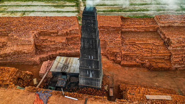 Brick factory operates with chimney releasing smoke over stacks of bricks in Dhaka, Bangladesh