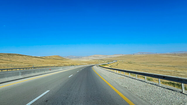 Long and winding road stretches through arid landscape in Northern Azerbaijan under clear blue sky