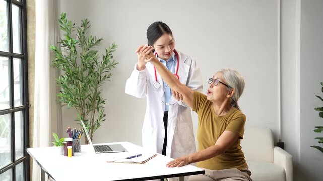 Asian female doctor providing physical therapy to an elderly woman, helping her with arm exercises and rehabilitation in a modern clinic for senior healthcare and recovery