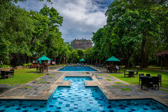 Hotel pool area surrounded by trees with view of ancient rock fortress in Sri Lanka