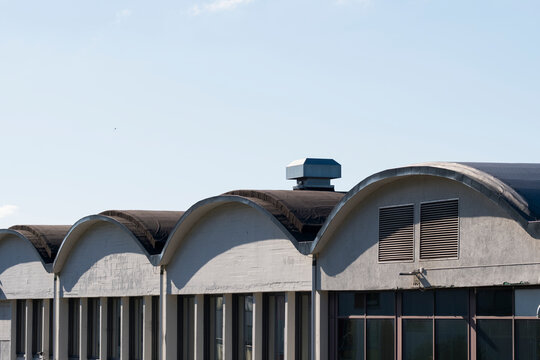 curved roof spans industrial exterior where columns and windows repeat across urban architecture under clear sky with geometric rhythm