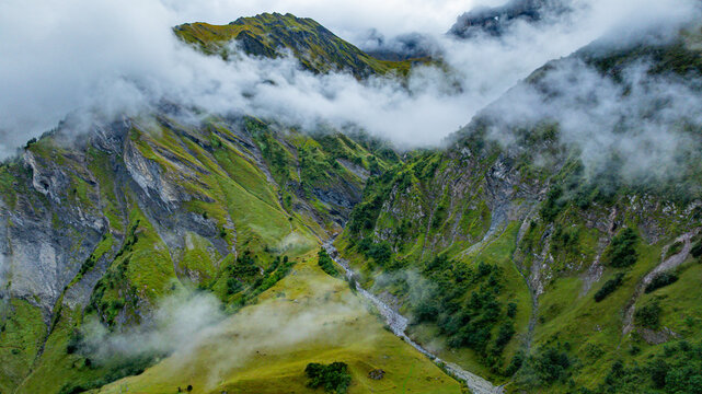 Clouds cover green mountains and rocky cliffs in Tschinglengorge during a misty day in Sardona National Park, Switzerland