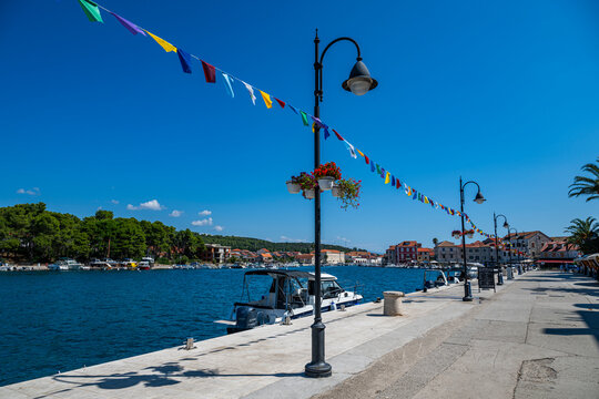 Colorful flags decorate the waterfront near boats in Stari Grad, while trees and buildings line the bay in Croatia