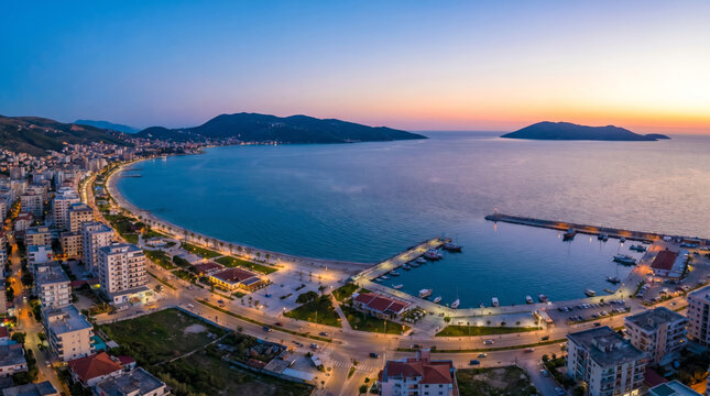 Panoramic view of a coastal city at sunset with a large bay and harbor filled with boats.