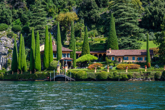 Villa La Cassinella shows lush greenery and gardens along the shoreline of Lake Como in Italy with cypress trees and a clear blue sky