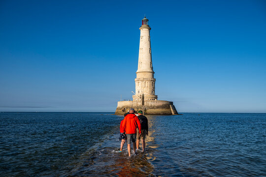 Visitors walk on the sand around the lighthouse of Cordouan during low tide in France