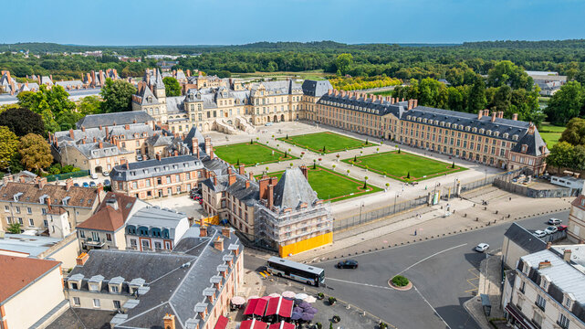 Aerial view showcasing Fontainebleau Palace and its gardens with surrounding buildings and roads during daylight in France