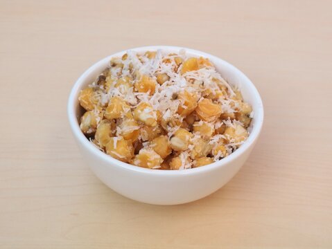 Urab Jagung or traditional indonesian sweet and savory snack made from boiled corn kernels mixed with fresh grated coconut, served in a clean white ceramic bowl on a wooden background