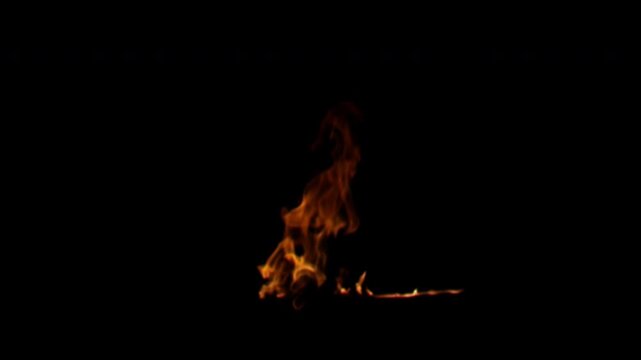Close up of a small bonfire with intense orange and yellow flames burning in the dark.