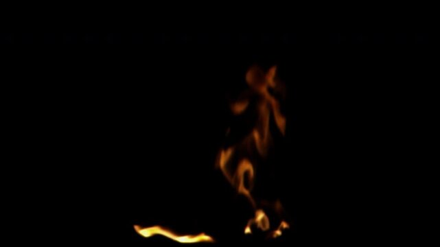 A small single flame burns brightly and flickers against a solid black background in slow motion.