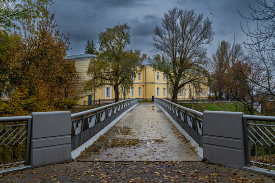 Visitors walk on a bridge toward a historic building in a park on a cloudy day in Gomel, Belarus