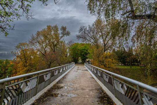 Bridge in Gomel park offers a view of trees and sky in autumn with grey clouds overhead in Gomel, Belarus