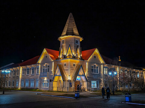 Town square of Naryan-Mar shines brightly at night with illuminated buildings and people walking in Nenets Autonomous Okrug, Russia