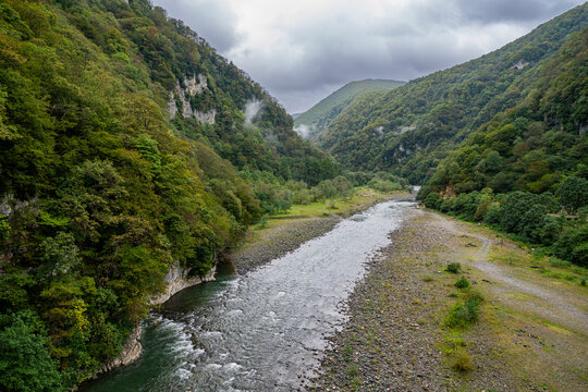 Lupshara river flows through a green valley in Ritsa Relict National Park with rocky banks and forested hills in Russia