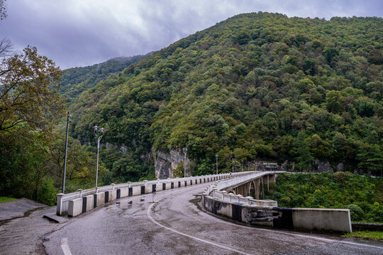 Bridge over Lupshara River in Ritsa Relict National Park surrounded by mountains and trees during an overcast day in Russia