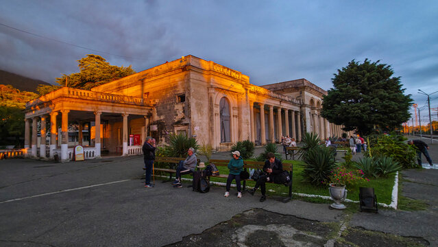 Gagra railway station shows people gathered near historic building during evening in Abkhazia with lights illuminating the scene