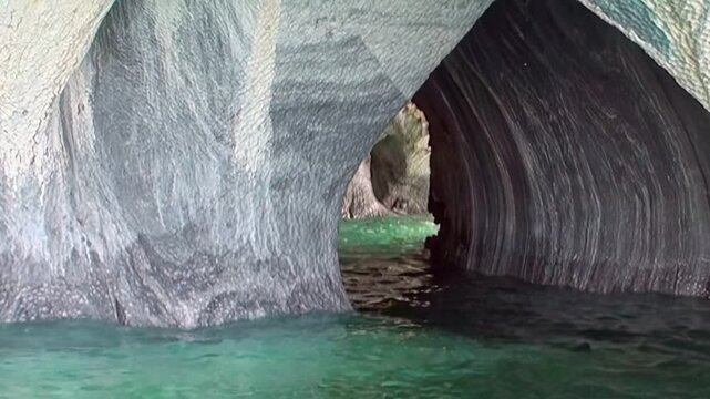 A serene journey glides through Patagonia's majestic Marble Caves. Witness nature's artistry where smooth, swirling marble walls meet dazzling turquoise waters on a bright day.
