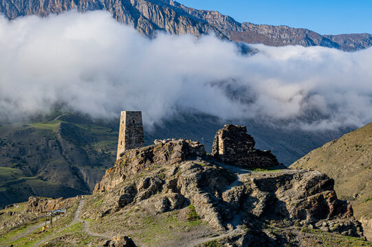 Old watchtower stands on hill overlooking mountains in North Ossetia, Russia during clear weather with clouds covering valley