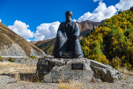 Statue of a poet sitting on a large stone with mountains and trees in the background in a quiet area of South Ossetia, Russia