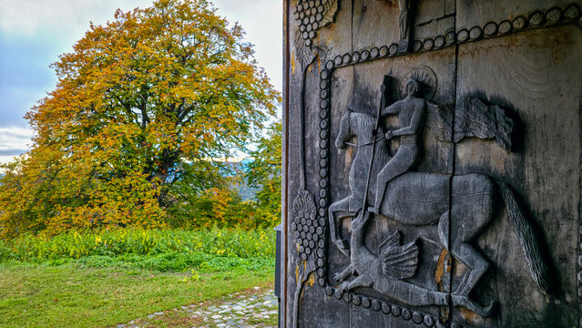 Wood carving door featuring horseback rider at St. George Church in South Ossetia, Russia, surrounded by nature and seasonal changes
