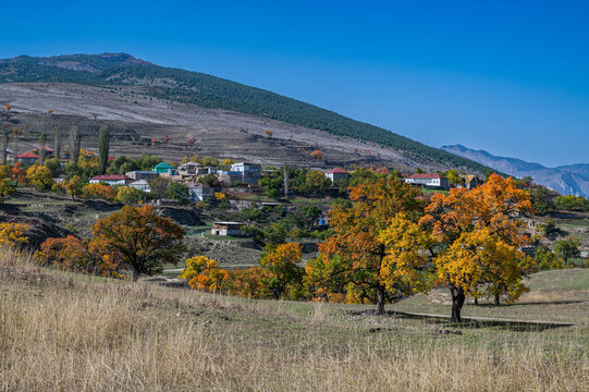 Colorful autumn trees overlook a quiet village in Dagestan, Russia during a sunny day in fall