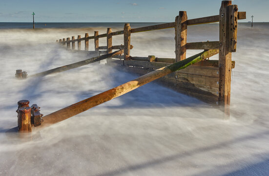 Waves crash around a groyne on the beach at Teignmouth, revealing the structure along the coast of the English Channel in Devon