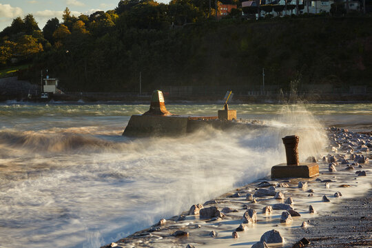 Surf crashes against the breakwater at the mouth of the River Teign in Devon during sunset
