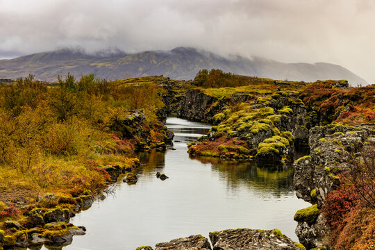 Water channel flows through volcanic rock at Thingvellir with clouds over Iceland's rift valley