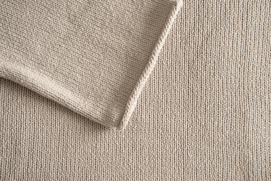 Knit pattern in beige wool fabric. Fine woven cotton texture with a folded sleeve for a decorative background. Close-up. Top view.