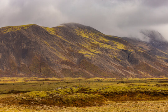 Mist covers mountains in Iceland revealing volcanic slopes with colors under dramatic clouds