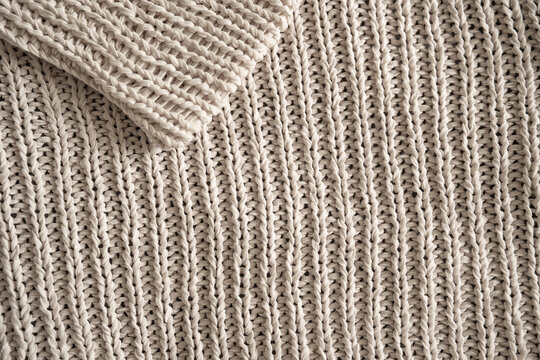 Knit pattern in beige wool fabric. Chunky woven cotton texture with a folded sleeve for a decorative background. Close-up. Top view.