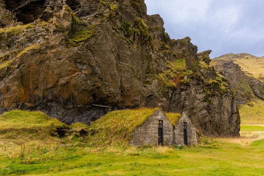 Historic turf-roofed stone houses built into cliffside near waterfall showcasing Icelandic architecture and landscape