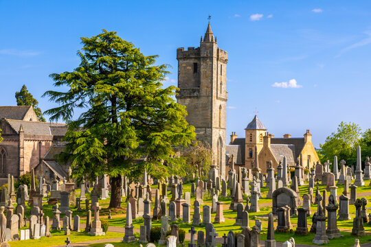 Church of the Holy Rude stands among gravestones in Valley Cemetery, Stirling, Scotland under a clear sky with trees in the foreground